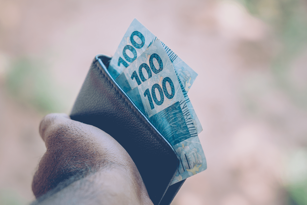 mão segurando carteira com notas de 100 reais aprendendo mais sobre educação financeira
