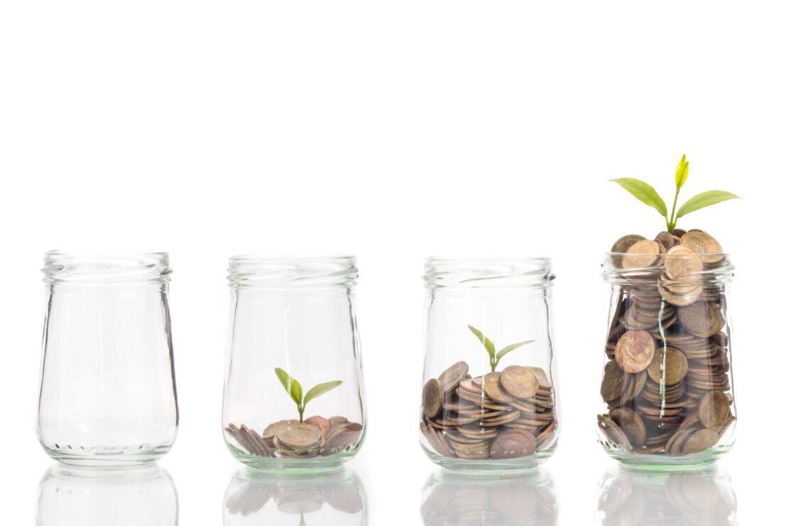 começar a investir: vidro com moedas dentro e uma muda de planta crescendo e o dinheiro multiplicando.