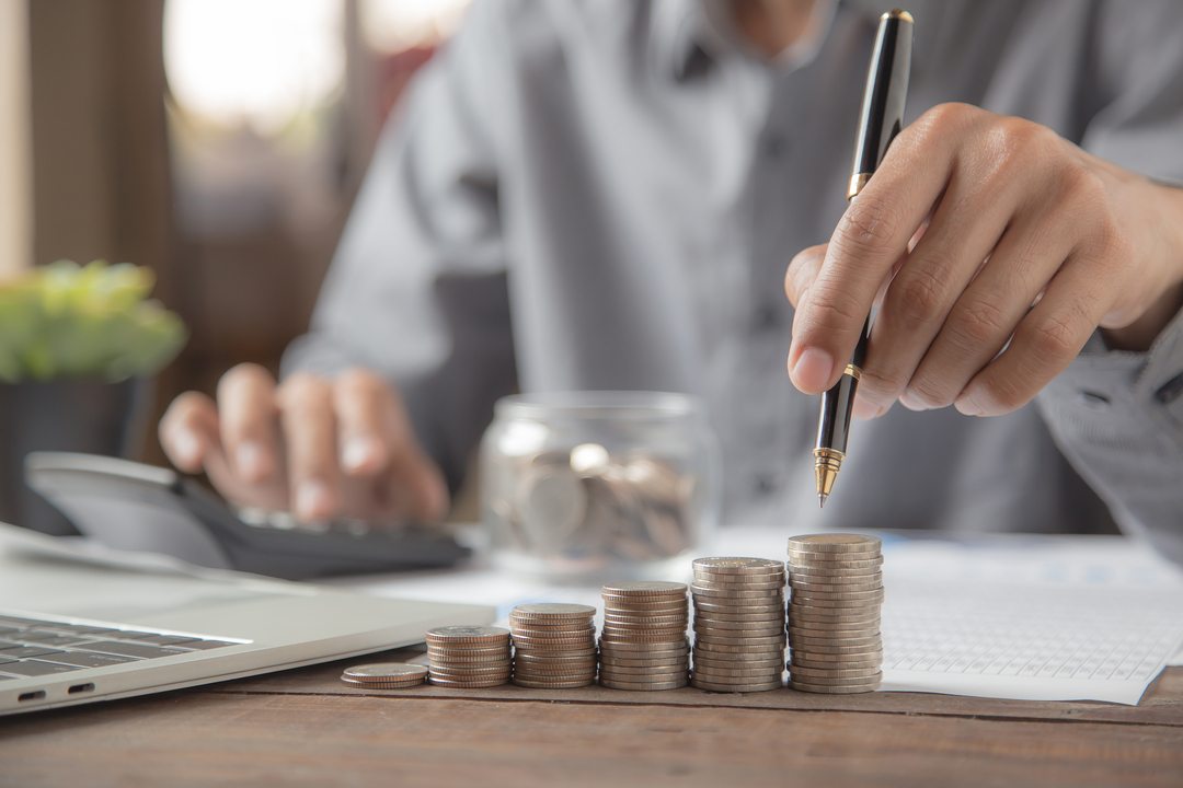 renda mensal ou resgate total: uma pessoa com uma caneta na mão e piramende de moedas crescentes sob a mesa.